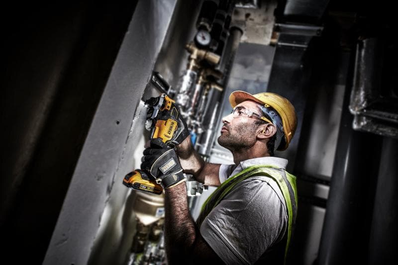 Ouvrier utilise un outil DEWALT DCS355D2 sur un mur, équipé de protections et de gants de sécurité.