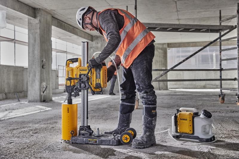 Ouvrier utilise une perceuse à béton DEWALT DCPS151 sur un chantier, équipé de protections et d'un casque.