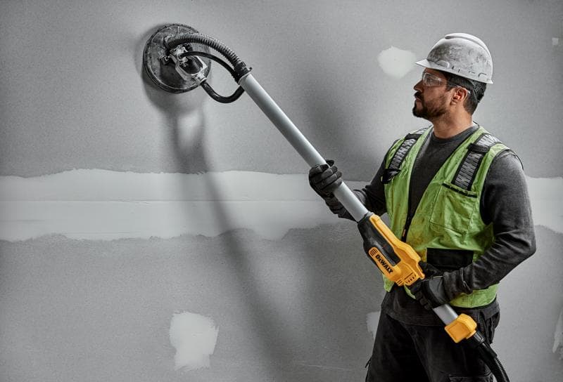 Ouvrier avec ponceuse murale DEWALT DWE7800, DWE7800-QS sur plaque de plâtre. Produit de photographie.
