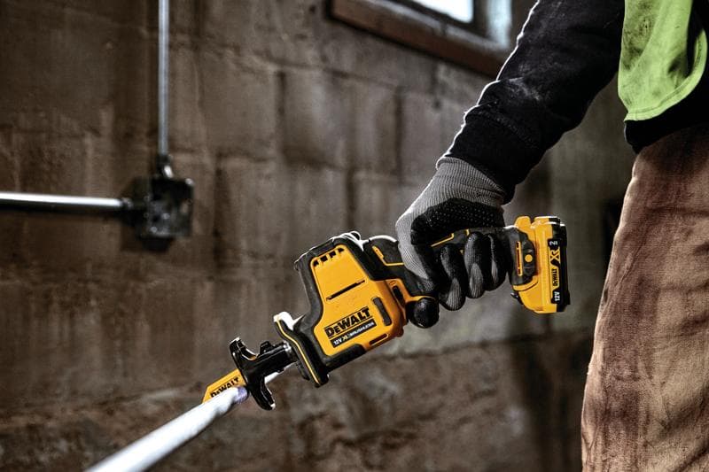 Main gantée tenant une scie sabre sans fil DEWALT DCS312D2 coupant un tuyau métallique en intérieur.