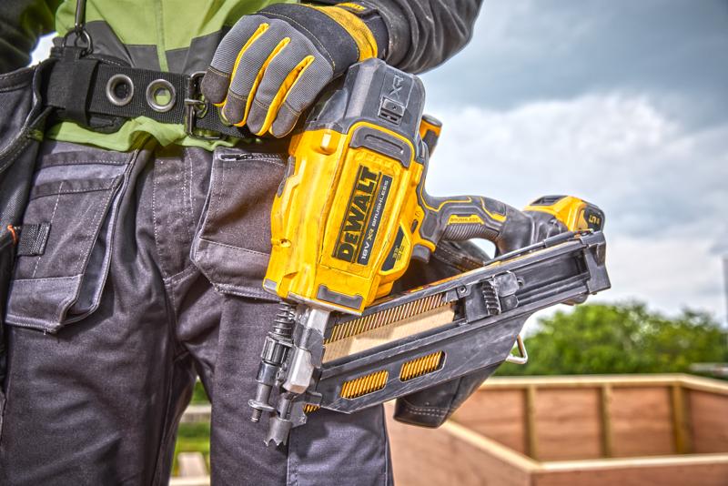 Personne tenant un cloueur DEWALT DCN930N, portant des gants et un équipement sur un chantier extérieur.