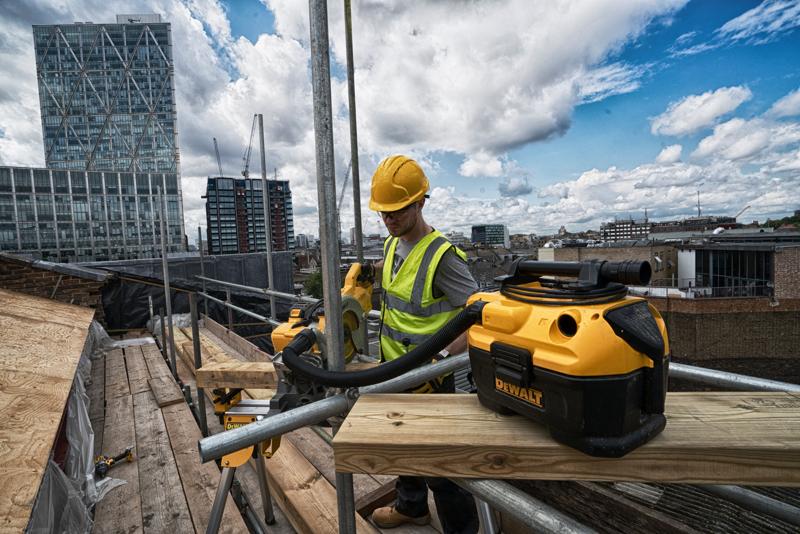 Aspirateur DEWALT DCV584 sur un chantier en hauteur avec un ouvrier équipé et des bâtiments urbains en arrière-plan.