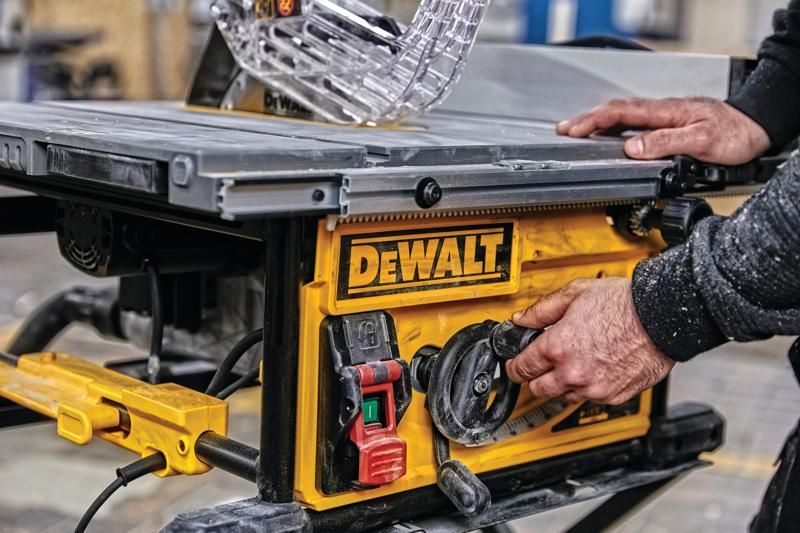 Gros plan d'une personne ajustant les réglages sur une scie à table DEWALT, avec un panneau de commande jaune comportant des interrupteurs et des cadrans, dans un atelier.